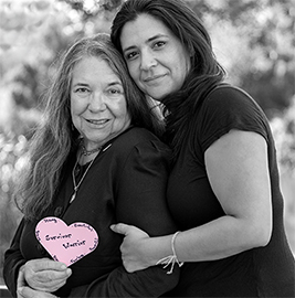 Mother & daughter together for breast cancer awareness; the mother holds a Project Pink heart with ‘Survivor Warrior’ on it